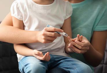 Mother holding her child and testing the child's blood suger levels with a finger prick tester