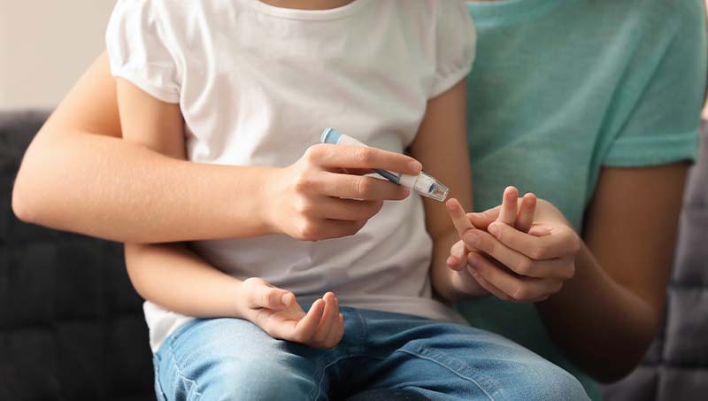 Mother holding her child and testing the child's blood suger levels with a finger prick tester